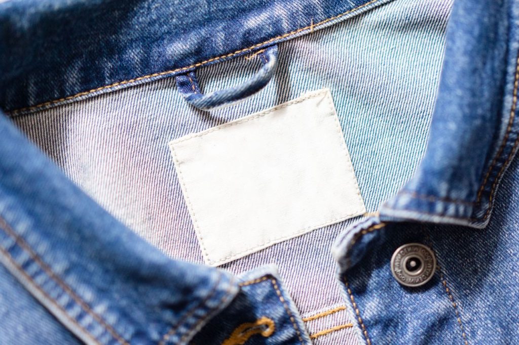 Close-up shot of a denim jackets collar featuring a blank white tag and detailed stitching.