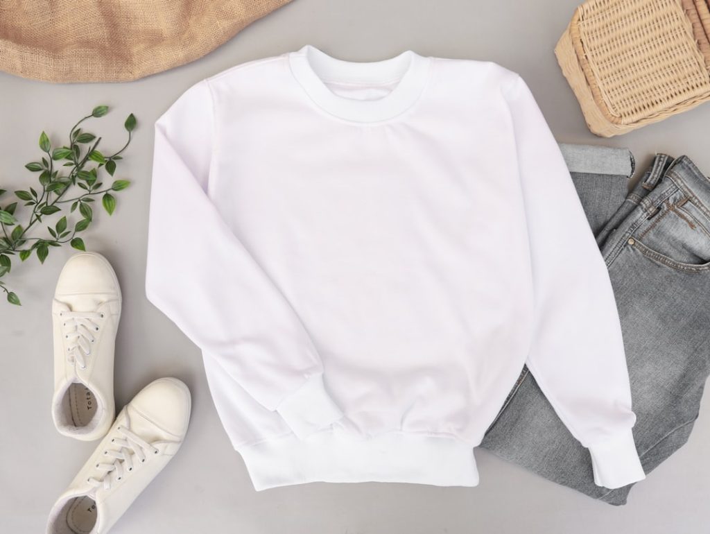 Blank and plain white sweater mockup photo with jeans and sneakers on the background. Use it to display your apparel design.